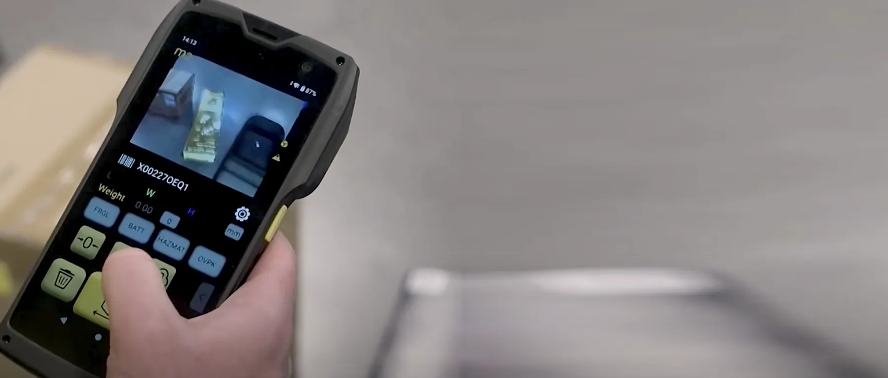 The M2 held in one hand over a box, its screen showing the live scan