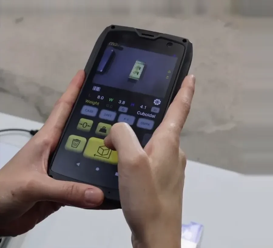 Hands holding the M2; the screen shows length, width, height and weight