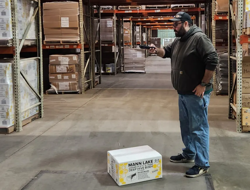 A worker measuring a boxed product in a warehouse aisle with the M2