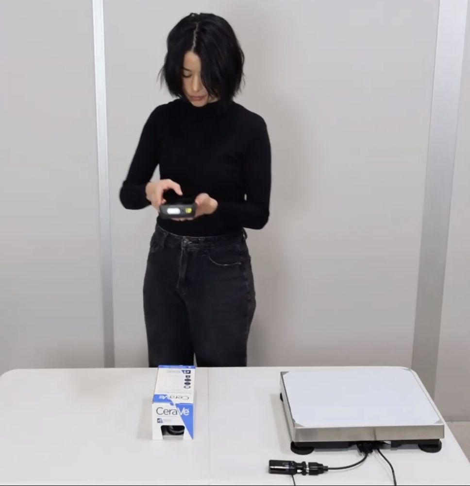 Operator at a bench measuring a boxed product with the M2, next to a scale
