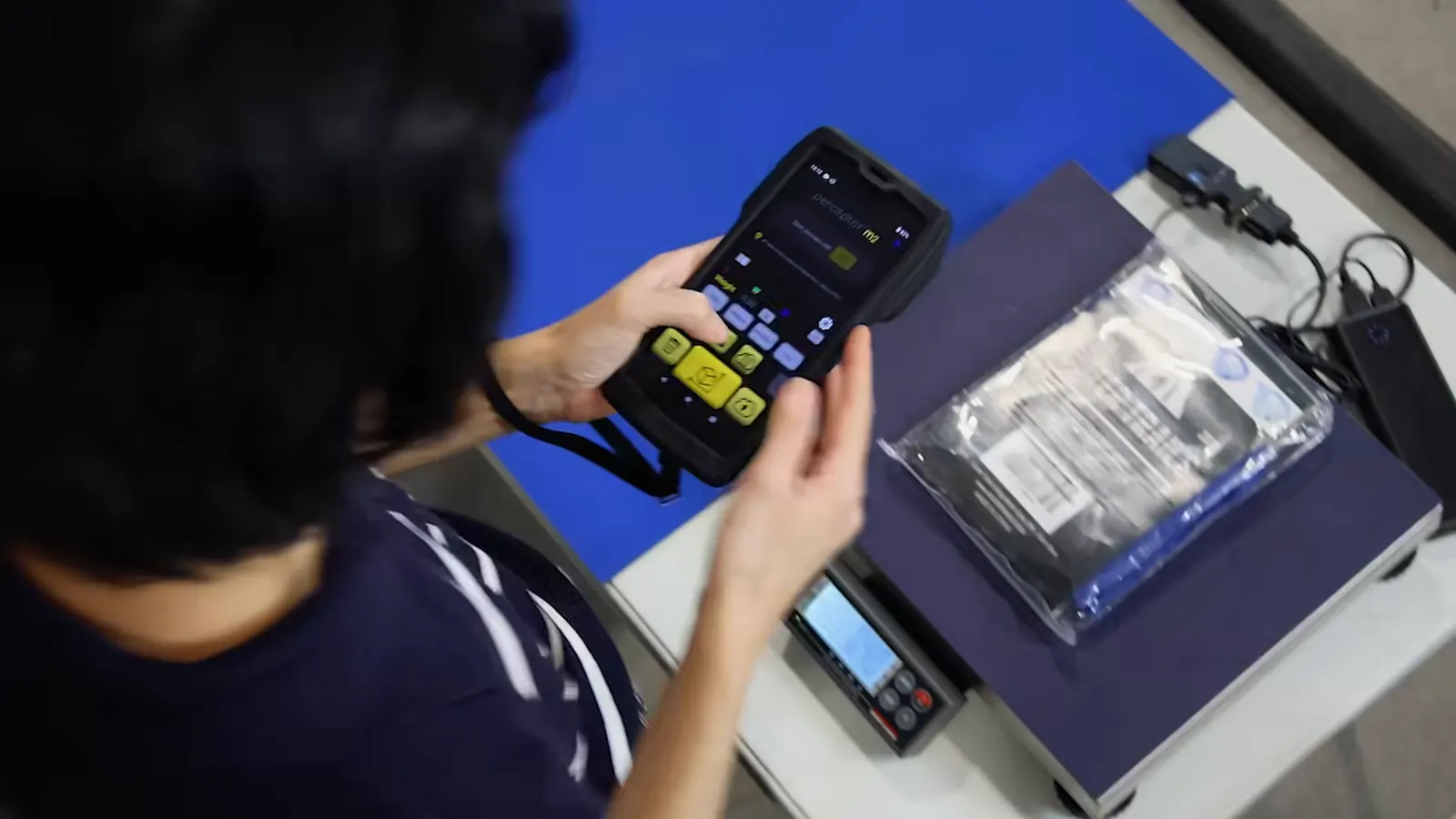 An operator holds the M2 over a polybag on a scale connected through the QBOID Bluetooth adapter